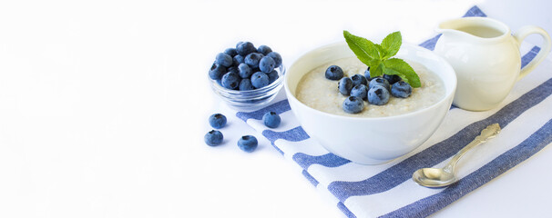 Oatmeal with milk and blueberry in the white bowl on the white background. Copy space.