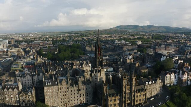 Aerial view of downtown Edinburgh buildings surrounded by lush countryside, featuring a tall chapel in the center.