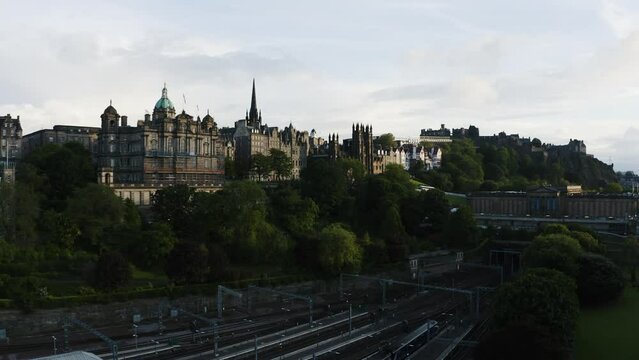 Rising aerial shot featuring Waverley Train Station, Museum on the Mound, and The Hub in Edinburgh, Scotland.