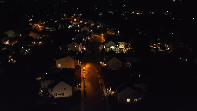 Lights illuminate large houses in upscale neighborhood in America at night. Aerial dolly forward shot of homes in development at dark.