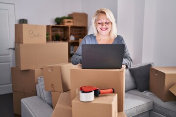 Middle age blonde woman smiling confident using laptop at new home