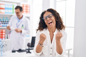 Middle age hispanic woman shopping at pharmacy drugstore celebrating surprised and amazed for success with arms raised and eyes closed