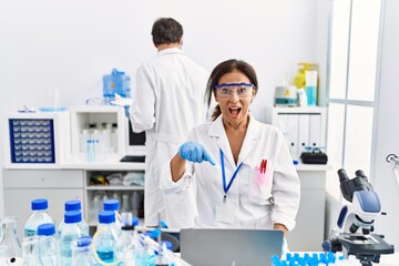 Middle age woman working at scientist laboratory smiling happy pointing with hand and finger