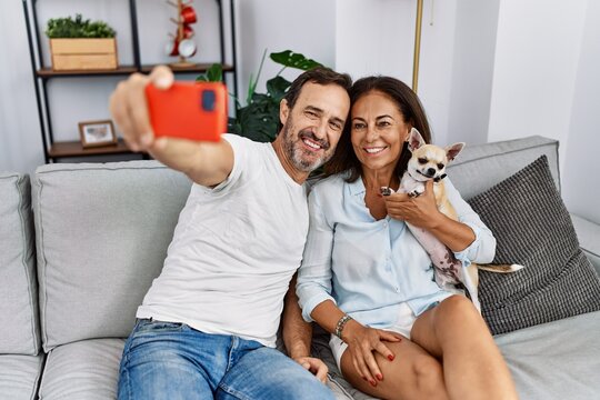 Middle age man and woman couple make selfie by the smartphone sitting on sofa with dog at home