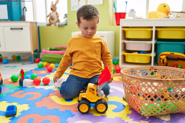 Adorable caucasian boy playing with tractor toy sitting on floor at kindergarten
