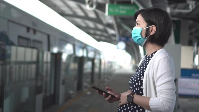 Young Asian Pregnant woman wearing blue protective face mask waiting for a train at train station, looking away