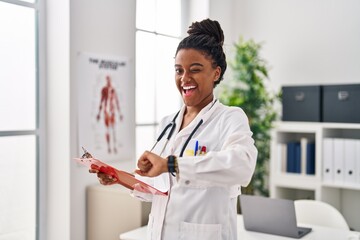Young african american with braids wearing doctor uniform looking at the watch winking looking at...