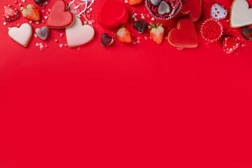Various Valentine day sweets and desserts, cookies, chocolates, candy, sugar sprinkles with strawberry on high-colored bright red holiday background flatlay top view copy space