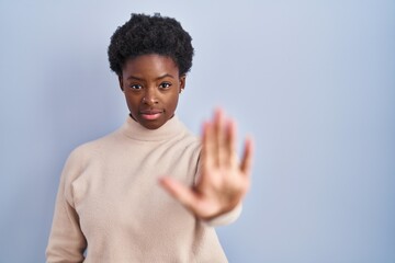 African american woman standing over blue background doing stop sing with palm of the hand. warning...
