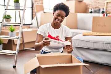 African american woman unpacking package sitting on floor at new home
