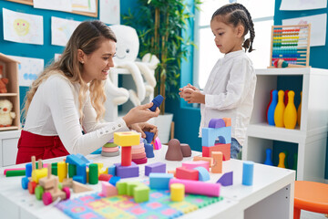 Teacher and toddler playing with geometry blocks sitting on table at kindergarten