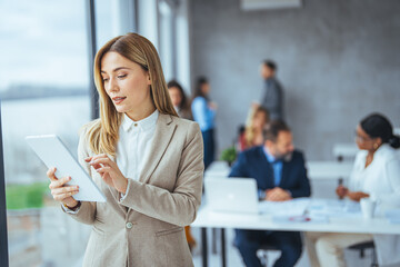 Obraz premium Waist up portrait modern business woman in the office with copy space. Female executive wearing businesswear standing outside modern meeting room and checking data on tablet.
