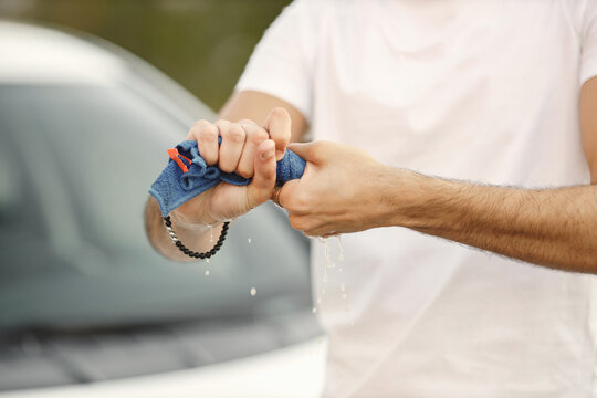 Cropped photo of a man's hands with a washcloth standing near his car