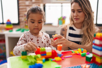 Teacher and toddler playing with construction blocks sitting on table at kindergarten