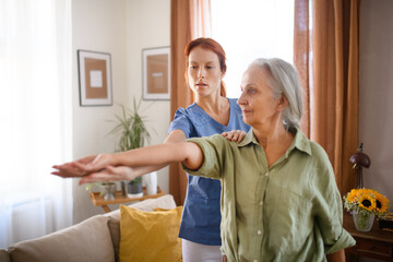 Nurse exercising with senior woman at her home, concept of healthcare and rehabilitation.