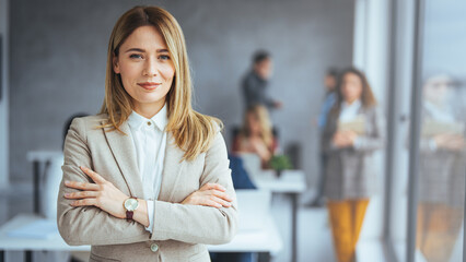Obraz premium Portrait of businesswoman with a file standing in meeting room with colleagues disucssing in background. Waist up portrait modern business woman in the office with copy space