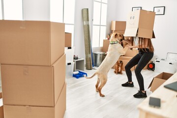 Young hispanic woman wearing funny cardboard on head playing with dogs at new home