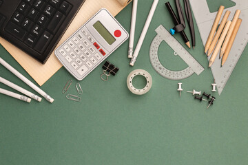stationery items around of image on green background. Back to school background, banner with copy space. Student's or engineer's supplies. Office objects on dark green background. Calculator, keyboard