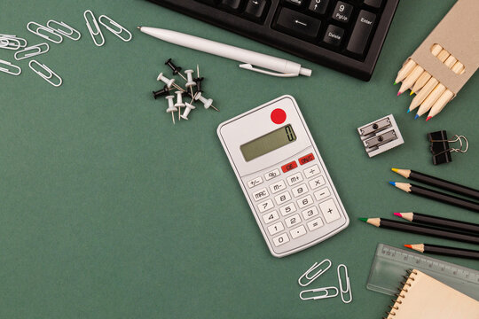 stationery items around of image on green background. Back to school background, banner with copy space. Student's or engineer's supplies. Office objects on dark green background. Calculator, keyboard