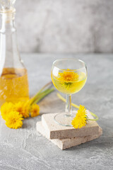 Dandelion homemade wine in a glass and bottle. Spring alcoholic drink. Light background.