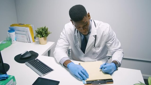 Black Stock Footage of millennial Black man wearing personal protective equipment PPE face masks and latex gloves while working in the hospital office at his desk