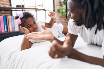 Father and daughter lying on bed speaking at bedroom