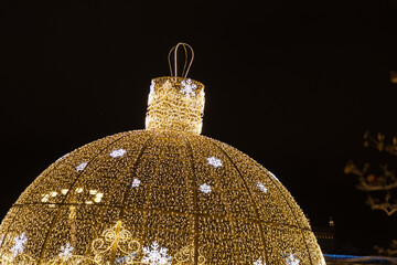 Giant Christmas ball decorated with garlands with ornaments glowing with lights on night city...