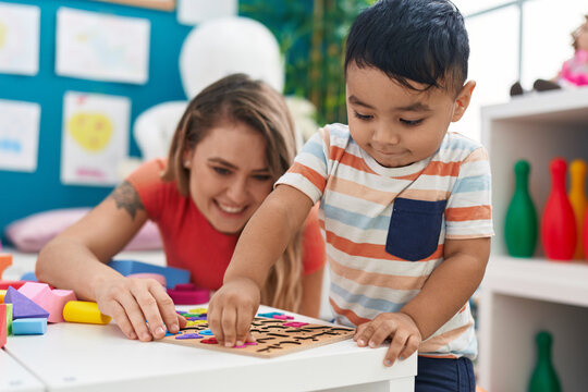 Teacher and toddler playing with maths puzzle game sitting on table at kindergarten