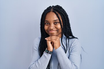 African american woman standing over blue background laughing nervous and excited with hands on...