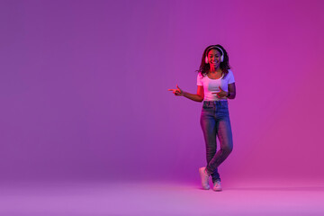 Happy Young Black Woman In Wireless Headphones Pointing Aside At Copy Space
