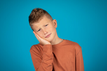 Unhappy preteen boy suffering from tooth ache, touching cheek with hand