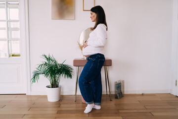 Pregnant woman touching belly while standing in apartment