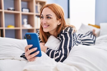 Young caucasian woman using smartphone lying on bed at bedroom