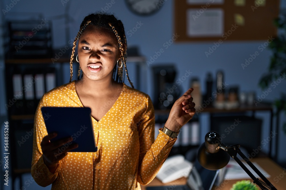 Canvas Prints African american woman with braids working at the office at night with tablet pointing aside worried and nervous with forefinger, concerned and surprised expression