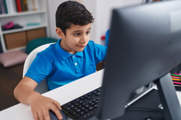 Adorable hispanic boy student using computer sitting on table at classroom