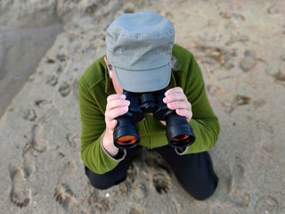 man looking through binoculars sitting on the sand, top view