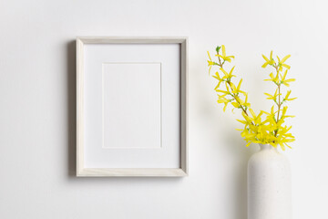 Vertical artwork frame mockup on white wall with yellow plant decor in vase