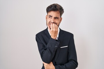 Young hispanic man with tattoos wearing business suit and tie looking stressed and nervous with hands on mouth biting nails. anxiety problem.
