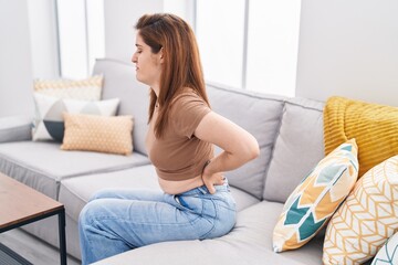 Young woman suffering for backache sitting on sofa at home