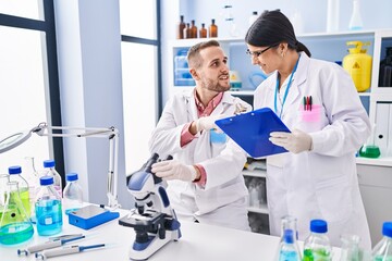 Man and woman wearing scientists uniform using microscope at laboratory