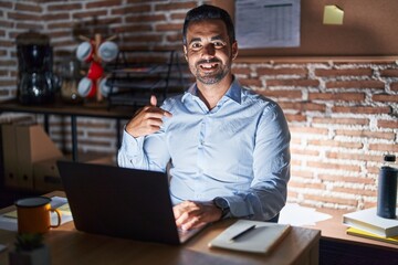 Hispanic man with beard working at the office at night looking confident with smile on face,...