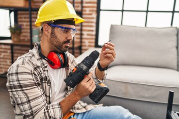 Young hispanic man worker smiling confident holding drill at home