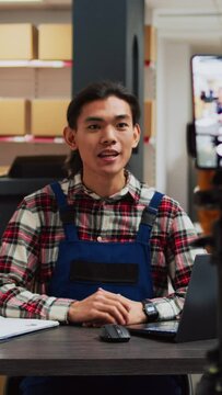 Vertical video: Male employee filming promotion video in warehouse, using social media streaming platform to promote small business in storage room. Young people doing teamwork for advertisement.