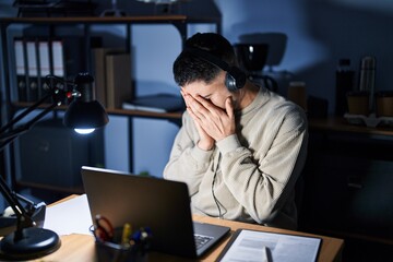 Young handsome man working using computer laptop at night with sad expression covering face with hands while crying. depression concept.