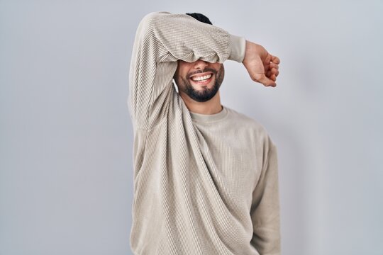 Young handsome man standing over isolated background covering eyes with arm smiling cheerful and funny. blind concept.