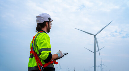 Male engineer in uniform looking at wind turbines in a windmill field