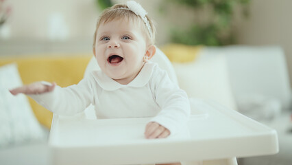 Adorable blonde baby smiling confident sitting on highchair at home