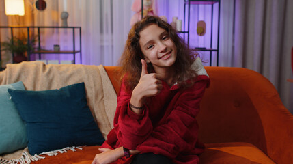 Like. Happy preteen young girl looking approvingly at camera showing thumbs up, like sign positive something, good great news, positive feedback. Adult child, kid sitting on couch at home living room