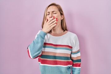 Young blonde woman standing over pink background bored yawning tired covering mouth with hand. restless and sleepiness.