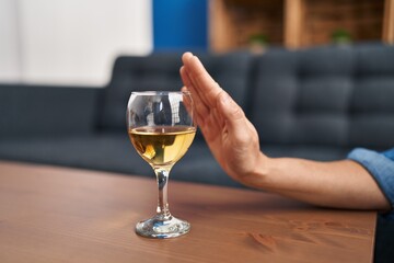 Young blonde woman rejecting glass of wine sitting on sofa at home